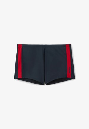 Námořnicky modré plavecké šortky s vertikálními červenými pruhy po obou stranách a malým logem na pravém pruhu, položeny naplocho na bílém pozadí.