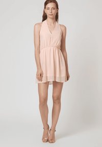 Vestido de cuello halter en suave gasa rosa, con cintura elástica y una falda fluida, complementado con tacones metálicos con tiras.