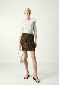 Top branco de manga longa, saia mini justa de padrão de leopardo, sandálias de salto bloco pretas e bolsa branca, contra um fundo neutro.