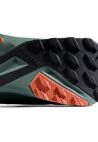 Trailrunning-Schuhsohle in Grün und Schwarz, ausgestattet mit auffälligen orangen Gummi-Traktionsnoppen und einer strukturierten Oberfläche für besseren Grip und Haltbarkeit.