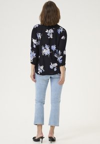 Blusa nera a fiori con fiori blu e bianchi, in tessuto leggero, maniche a tre quarti e vestibilità comoda, abbinata a jeans azzurri chiari.