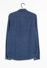 Chemise bleue à manches longues en tissu texturé, avec un col chemise et un ourlet arrondi. Comprend des poignets boutonnés et un cintre pour l'exposition.
