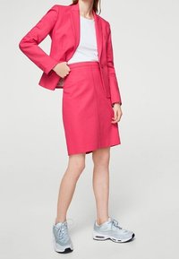 Blazer rose associé à une jupe rose et un t-shirt blanc ; accentué par des baskets bleu clair avec une texture lisse et un design arrondi.