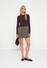 Langärmliges bordeauxrotes Oberteil, kombiniert mit einem karierten Minirock in Braun- und Beigetönen, abgerundet mit schwarzen Ballerinas und einer schwarzen Clutch.