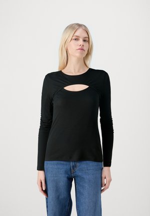 Black long-sleeve top in ribbed fabric featuring a front cut-out detail and gathered sides, paired with blue wide-leg jeans.