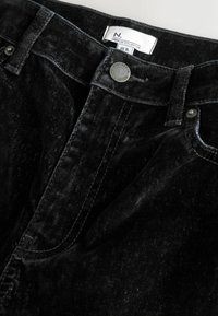 Blugi din denim negru cu o textură moale, având închidere cu nasture și o etichetă. Materialul are variații subtile în culoare și finisaj.