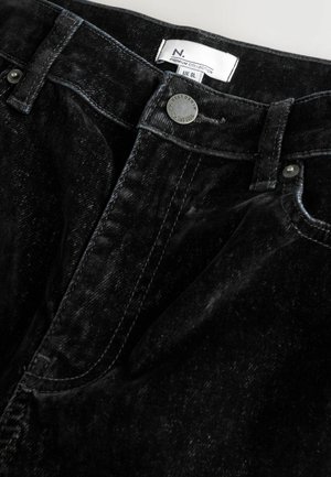 Čierne džíny z denimu s jemnou textúrou, s uzatváraním na gombík a etiketou. Materiál má jemné variácie v farbe a povrchovej úprave.