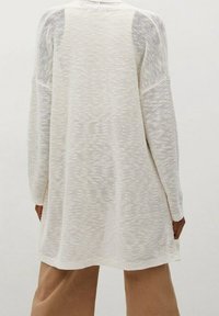 Keve könnyű, kötött pulóver törtfehér színben, laza szabású, texturált mintával és eső vállakkal, térd közepéig érő hosszal.