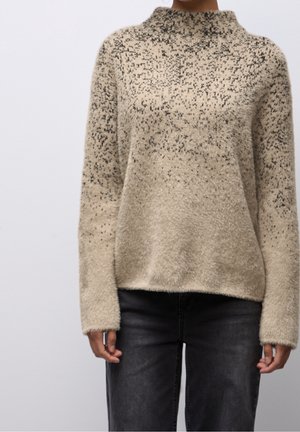 Beige fuzzy sweater with a high collar and speckled dark brown pattern worn with dark gray jeans on a person.