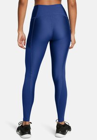 Leggings azules de cintura alta, hechos de una tela elástica con costuras en contraste; combinados con zapatillas deportivas negras y un panel trasero texturizado.