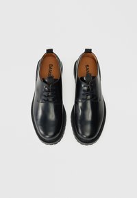 Schwarze Leder-Schnürschuhe mit runder Zehenpartie, strukturiertem Gummisohle und Zuglasche an der Ferse. Das Innere verfügt über ein beiges Futter.
