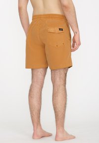 Shorts de color mostaza con una cintura elástica, un bolsillo trasero y detalles de costura, mostrados desde una vista trasera.