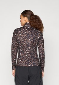 Hosszú ujjú leopárdmintás felső barna és fekete árnyalatokban, magas gallérral és testhezálló szabással, rugalmas, texturált anyagból készült.