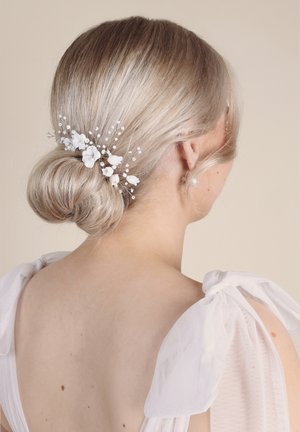 Accessorio per capelli con accenti floreali bianchi, perline delicate e chiusure in argento, acconciato in un elegante chignon su capelli chiari e texturizzati.