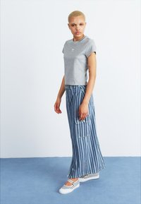 T-shirt de algodão cinza combinado com calças cargo largas listradas em azul com bolsos frontais, utilizadas com sapatos plataforma listrados em branco.