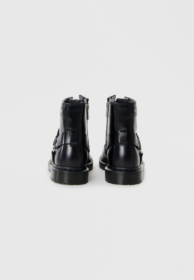 Bottines en cuir noir avec une finition lisse, dotées d'une fermeture éclair sur le côté, d'une semelle en caoutchouc et de sangles décoratives pour plus de détails.