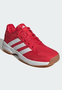 Chaussure de sport rouge avec une tige en mesh, trois rayures blanches et une semelle en caoutchouc naturel ; bout arrondi et conception à lacets.