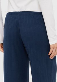 Námořnické modré ribbed kalhoty s elastickým pasem, které mají jemnou strukturu a pohodlný střih. Zadní pohled ukazuje hladké detaily látky.