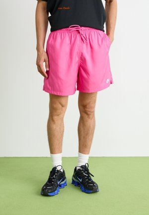 Rosa Badehosen mit elastischem Bund und Kordelzug, ausgestattet mit Seitentaschen und einem kleinen weißen Nike-Logo. Getragen mit schwarzen Schuhen.