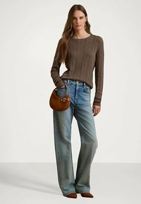 Γυναίκα φορώντας καφέ πλεκτό πουλόβερ, ανοιχτό μπλε παντελόνι σε φαρδύ στιλ, καφέ μυτερές γόβες, κρατώντας μια καφέ δερμάτινη τσάντα.