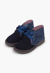 Botas de tobillo de ante azul marino con parte superior de textil brillante en azul, que presenta un gran lazo de cinta de satén y una suela de goma marrón con costuras en contraste.