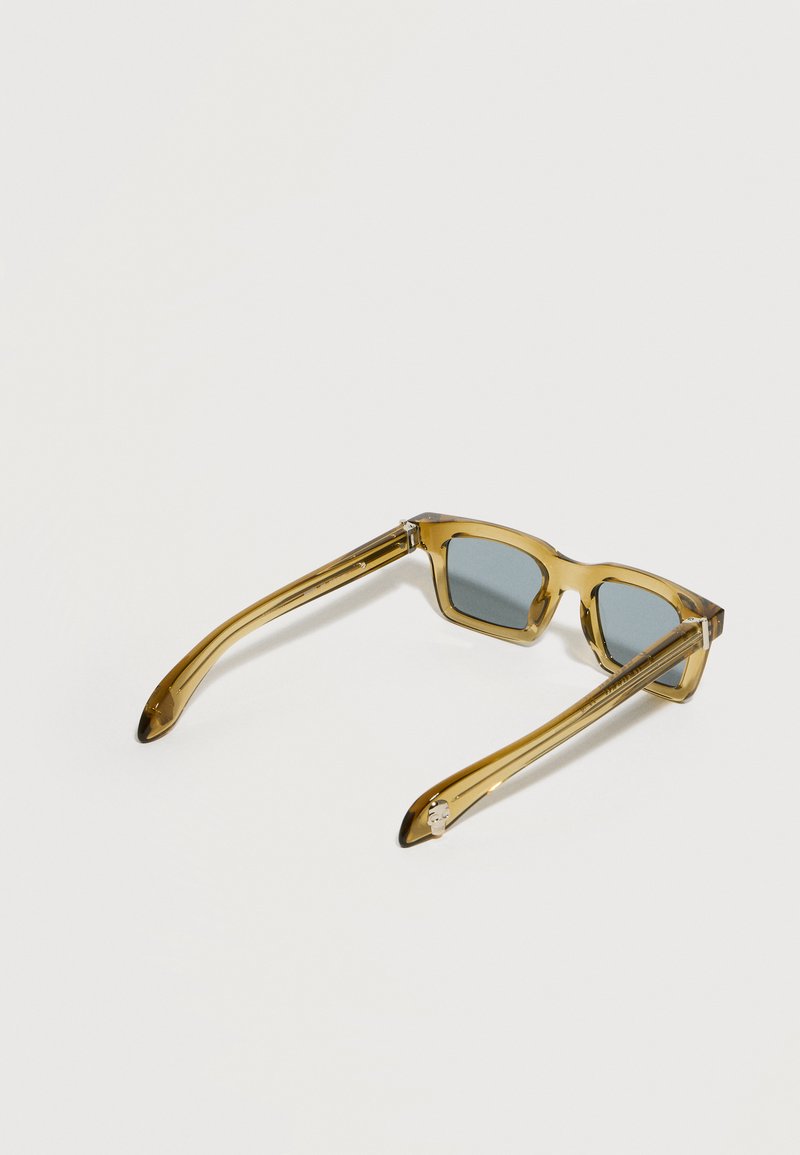 Transparent amber rectangular sunglasses with dark tinted lenses, resting open on a pale neutral background.