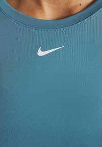 Camiseta deportiva de color azul verdoso, hecha de una tela suave, con cuello redondo y un pequeño logo de Nike blanco en la parte superior del pecho.