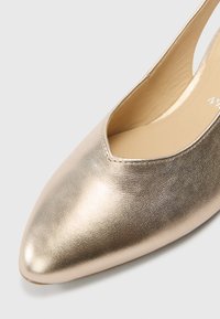 Metallisk guld slingback-sko med spids tå og åbne sider. Glat lædertekstur med minimal syning og enkelt design.