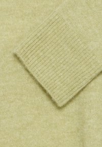 Gros plan sur le poignet d’un pull en laine beige avec une texture côtelée sur la manche, sur un fond en tissu de laine lisse.
