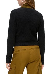 Pull noir texturé avec un design court et un ourlet côtelé. Porté avec un pantalon cargo de couleur moutarde doté de poches latérales et d'accents à rabat.