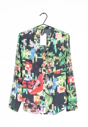 Langærmet skjorte med knapper og farverigt pixeleret mønster, der viser sommerfugle og blomsterdesigns, hængende på en sort bøjle.