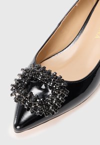 Schwarzer Lackleder-Stiefel mit spitzer Zehenpartie, der ein auffälliges schwarzes Strassverzierung in der Zehenpartie aufweist, und mit einer glatten beigen Fütterung.