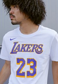 Hvid bomulds T-shirt med "LAKERS" i lilla med gul kant og nummer "23" i gul og blå mesh-mønster.