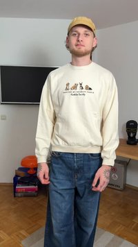 Φούτερ σε κρεμ απόχρωση με γραφικά ζώων και κείμενο, συνδυασμένο με φαρδιά μπλε τζιν παντελόνια. Υλικό από βαμβάκι, με ριμπ μανσέτες και μέση.