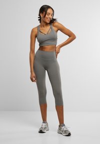 Grey athletic set featuring a cropped tank with crisscross straps and high-waisted capri leggings, both in a smooth, stretchy material.