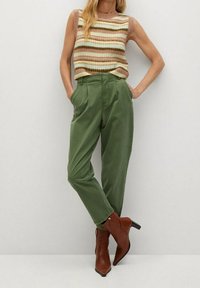 Pantalons taille haute verts avec des plis, associés à un haut sans manches en tricot rayé de couleur rose, verte et beige. Bottines à talons marron.
