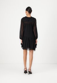 Μαύρο κοντό φόρεμα με δι�ακριτικά μακριά μανίκια, ριγμένο στρίφωμα και πλισέ μπούστο. Λείο υφασμάτινο με στρωτή σχεδίαση και μίνιμαλ σιλουέτα.