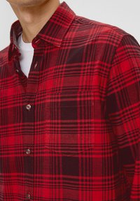 Rood en zwart geruit flanellen shirt met knoopsluiting aan de voorkant, een enkele borstzak en kraag. Gestructureerde stof met contrasterende patronen.