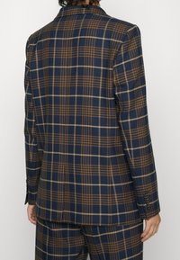 Námořnický a hnědý kostkovaný blazer se strukturovaným tvarem, klopovými límci a zapínáním na dva knoflíky. Má podrobné švy a rukávy na knoflíky.