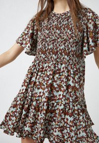 Blommig klänning med korta ärmar, med en smockad bål och lager på lager volangkant, i bruna, krämfärgade och gröna nyanser. Lättviktigt tyg.