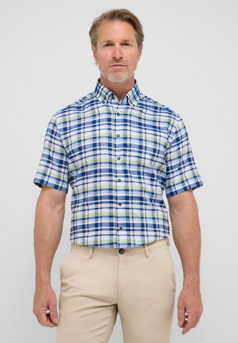 Camicia a maniche corte a quadri blu, verde e bianco; presenta bottoni e colletto; abbinata a pantaloni beige.