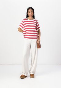 Camiseta de rayas rojas y blancas con mangas cortas, combinada con pantalones anchos blancos y zapatos de plataforma marrones. Bolso bandolera marrón.