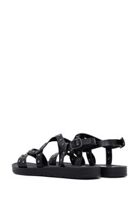 Zwarte leren sandalen met meerdere kruisende banden, metalen studs en een verstelbare gesp. Gladde en gestructureerde details op de banden.