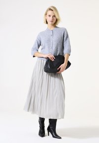 Cárdigan gris de punto con mangas tres cuartos, falda midi plisada plateada y bolso de mano negro, combinado con botas de tacón negras.