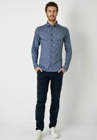 Marineblaue Langarmshirt mit Paisleymuster, Knopfleiste und strukturiertem Stoff, kombiniert mit dunklen Hosen und weißen Sneakers.