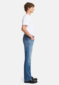 Jean en denim bleu clair avec une coupe droite, présentant un design classique à cinq poches et des détails de couture subtils. Associé à un T-shirt blanc.