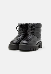 Black ankle boots with a glossy finish, featuring a quilted design, padded collar, and thick, patterned rubber sole. Adjustable laces on top.