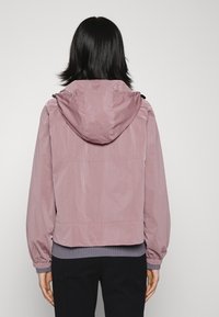 Light pink hooded jacket with a textured finish, elastic cuffs, and a ribbed hem. Features a casual fit and drawstring hood detail.