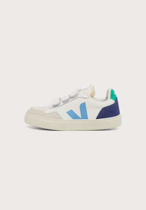 Baskets blanches avec logo bleu "V", bout beige, talon marine, languette de talon verte et trois bandes velcro blanches sur fond blanc.