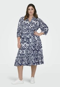 Mornarsko modra in bela obleka s kratkim ovratnikom, rokavi do tri četrtine in krilom v plasteh; kombinirana z belimi supergami.